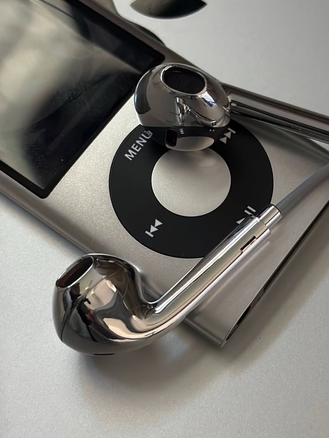 Close-up of a mirror-chrome Chrome Buds earbud resting on the click wheel of a silver iPod